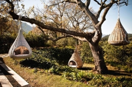 Lounge chair/shelter resembling a large bird’s nest shown hung from the trees.